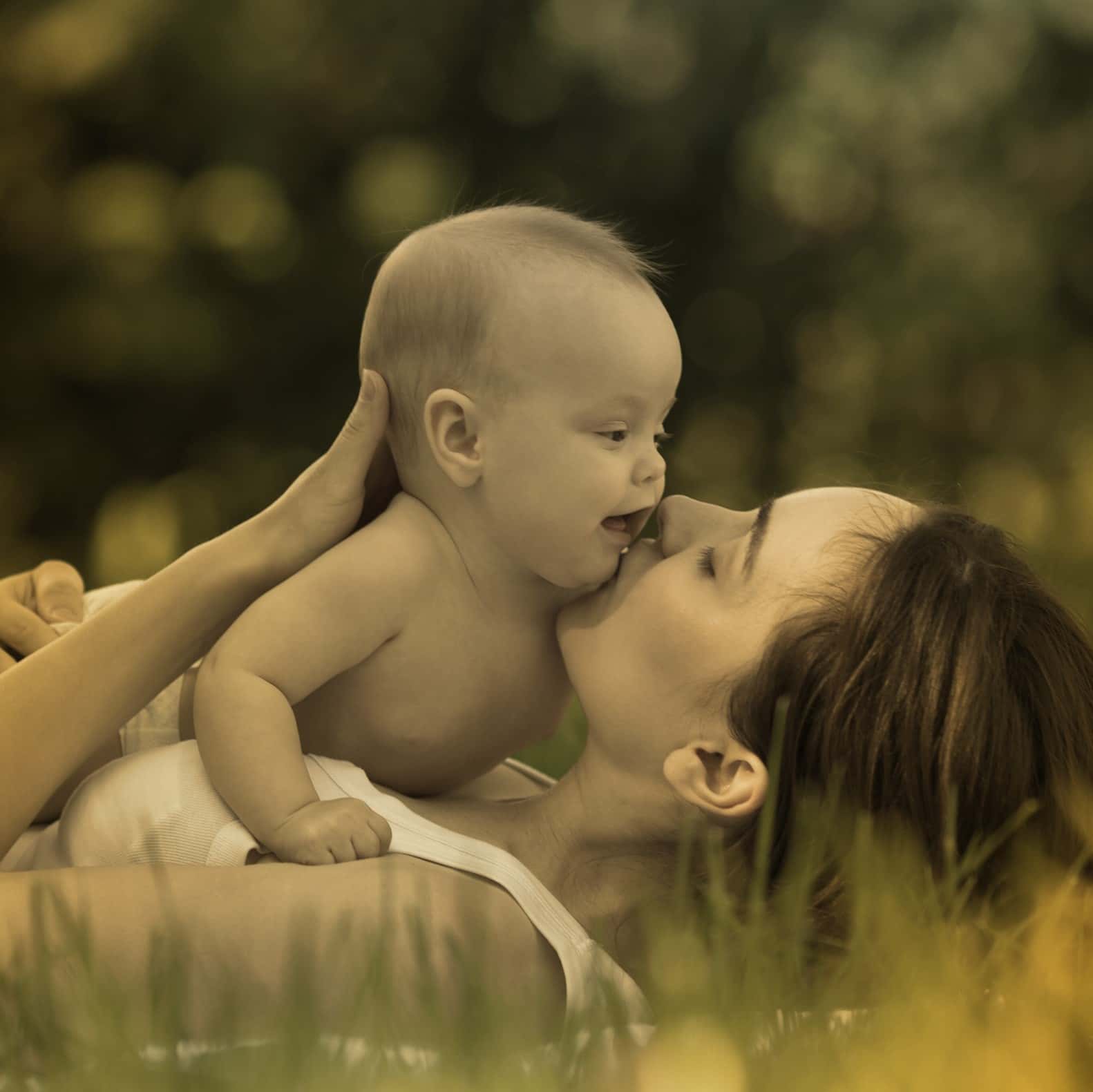 Eine Frau liegt auf der grünen Wiese und ihr Baby liegt auf ihrem Bauch